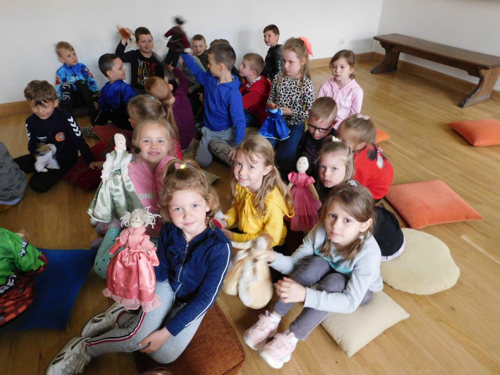 Dzieci siedzą, pokazując szmaciane lalki.