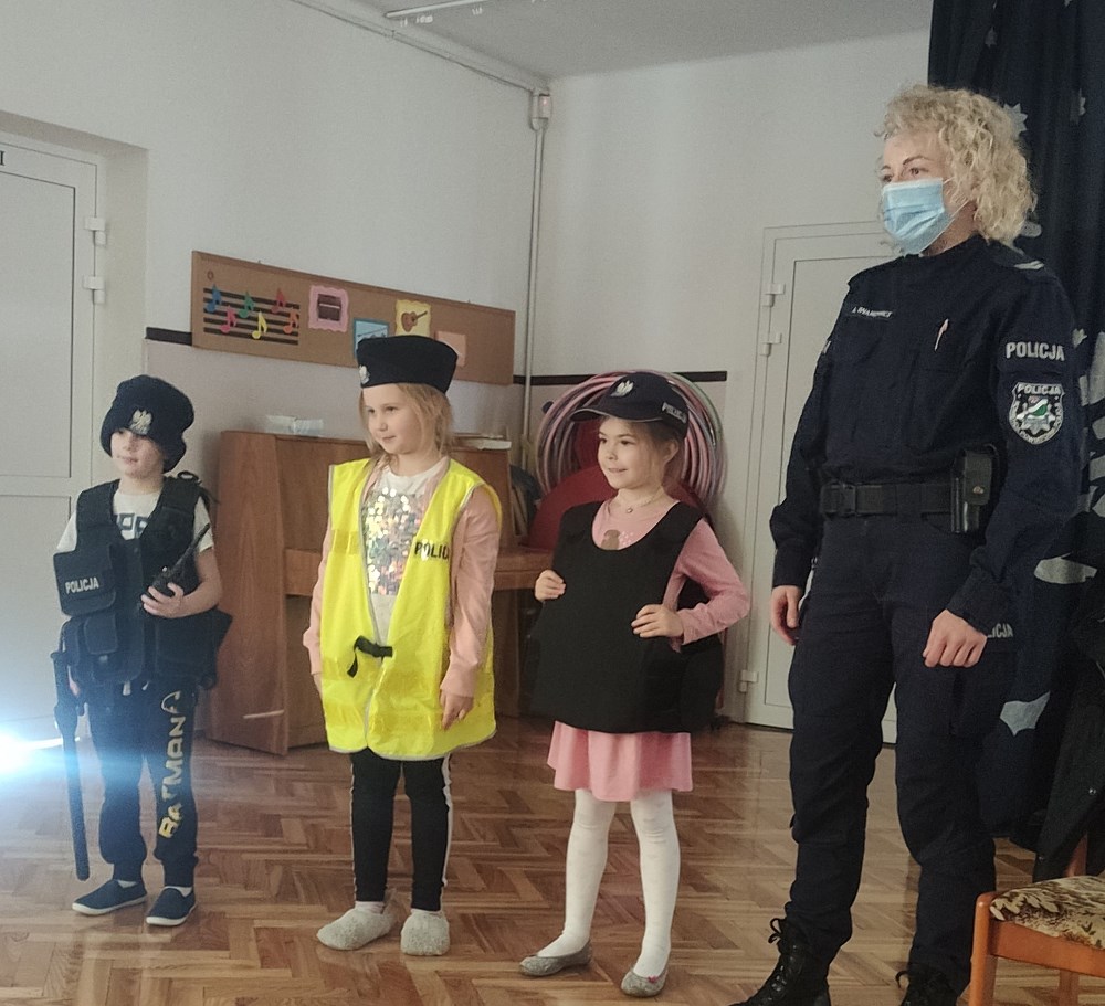 Troje dzieci z policjantką prezentują policyjne wyposażenie.