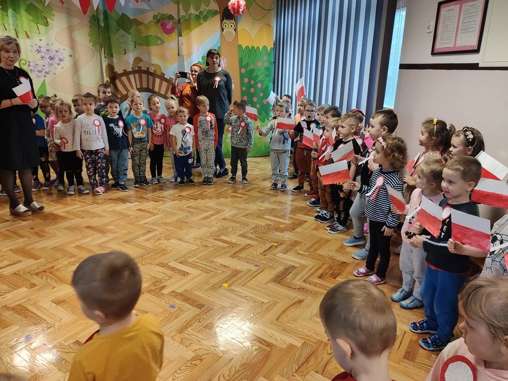 Grupa dzieci z flagami i kotylionami śpiewa Hymn Polski
