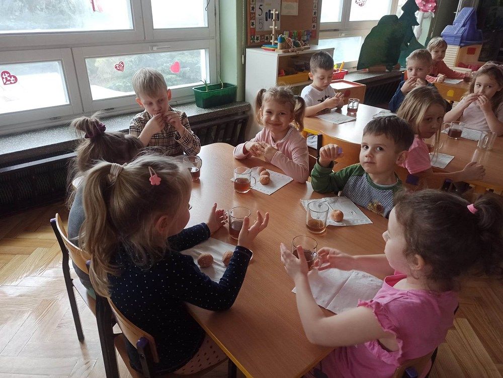 Dzieci przy stoliku jedzą pączki.