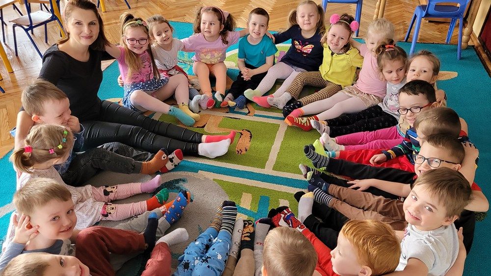 Dzieci siedzą w kręgu i prezentują stopy w kolorowych skarpetkach.