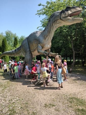 Dzieci pozują przed wielką rzeźbą dinozaura.