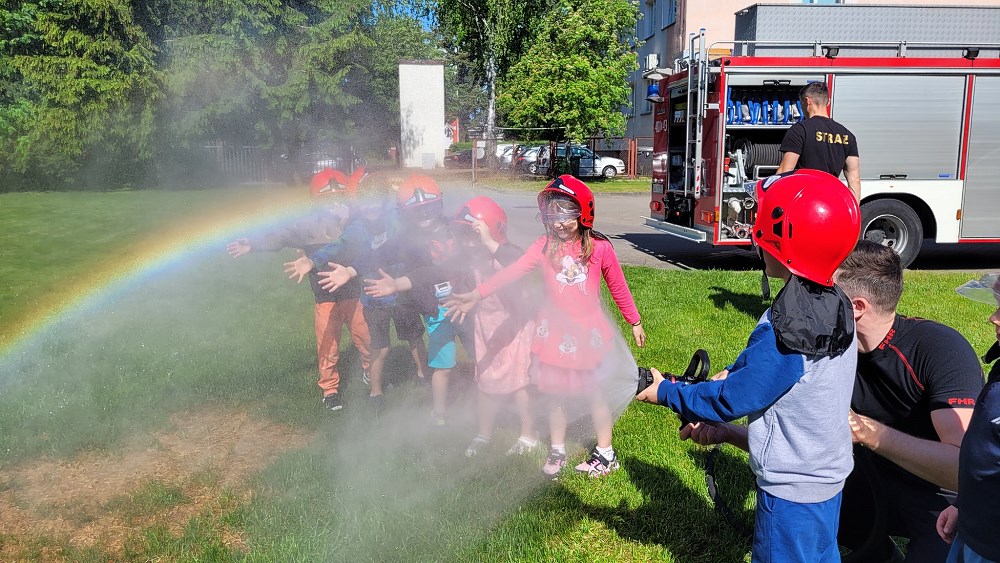Dzieci leją wodę z węża strażackiego.